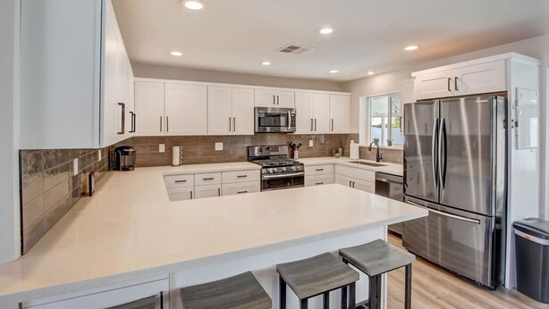 A modern kitchen with white cabinets, stainless steel appliances, and a central island with bar stools. - Family Retreat By Old Town w Pool (Phoenix)