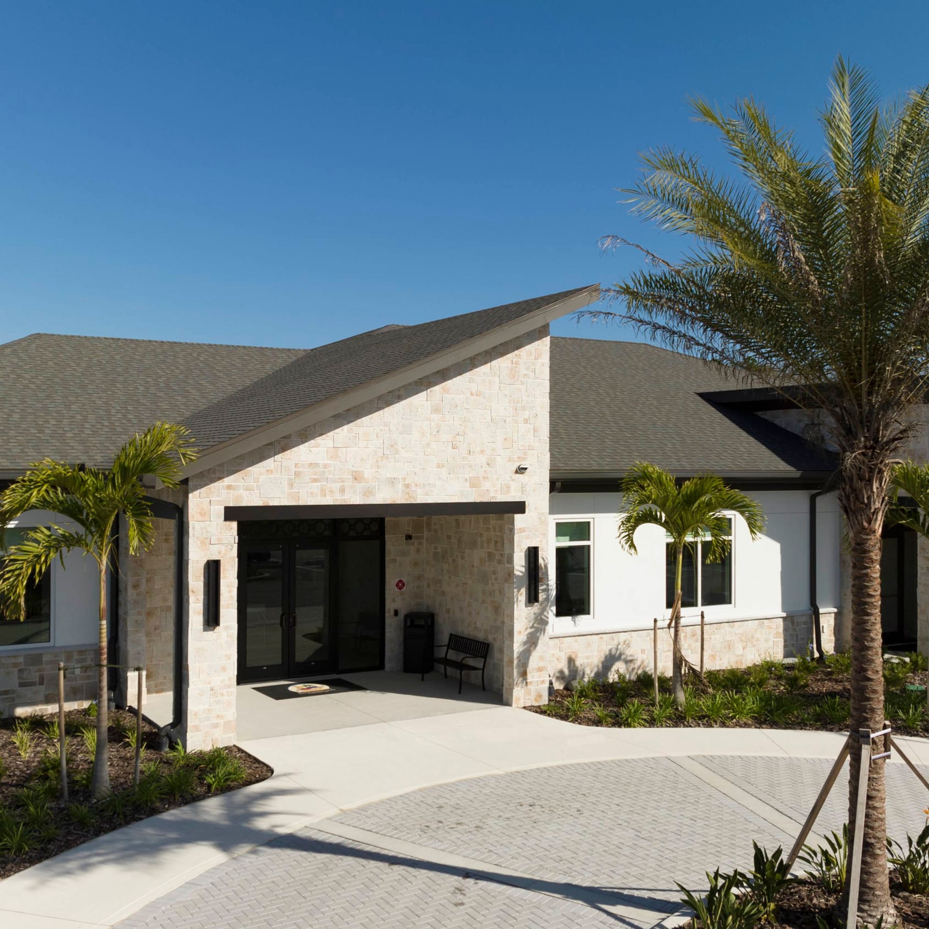 A modern building with a stone facade, a covered entrance, and palm trees in the foreground.