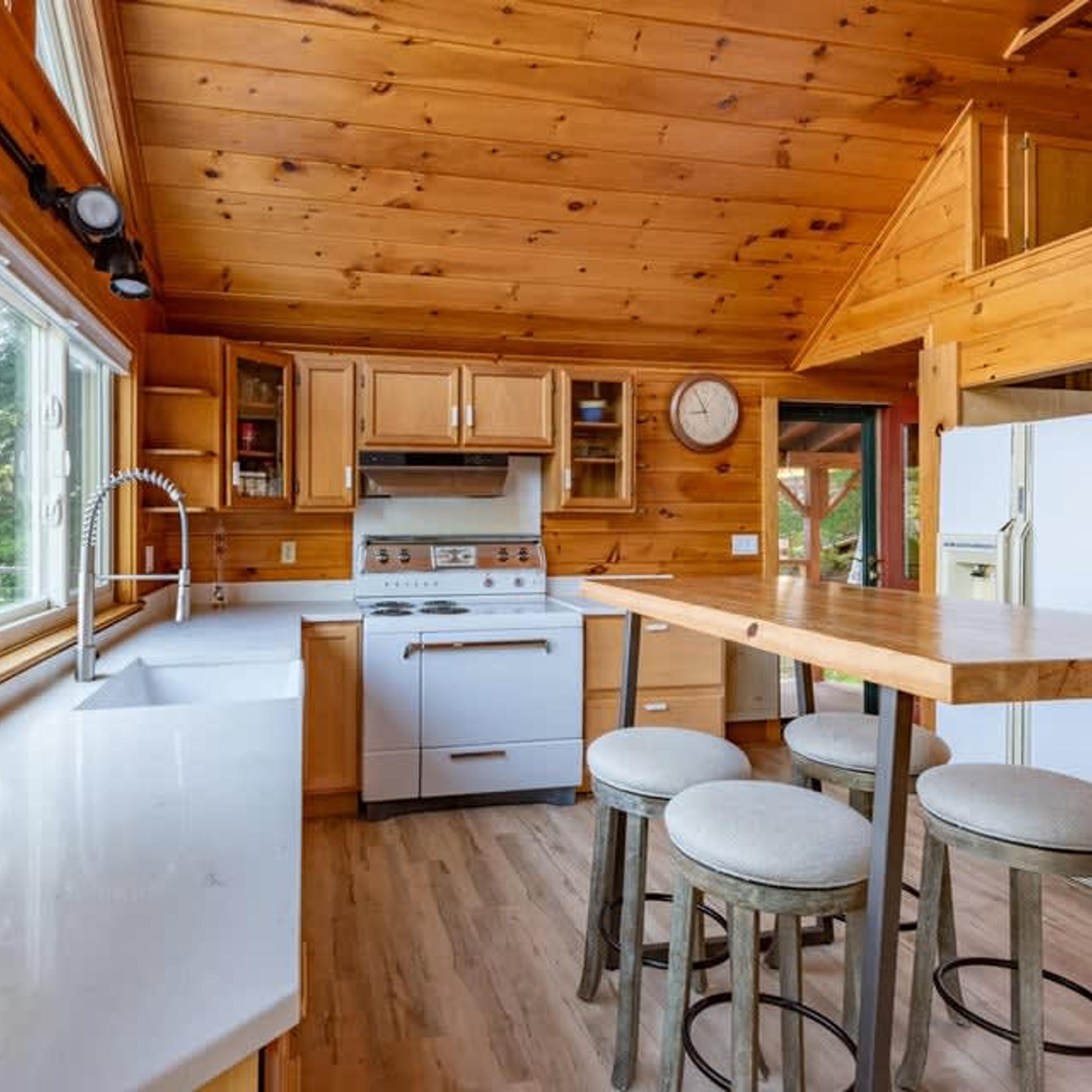 Una cocina compacta con armarios de madera, estufa, lavabo y un rincón con taburete.