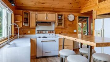 Una cocina compacta con armarios de madera, estufa, lavabo y un rincón con taburete.