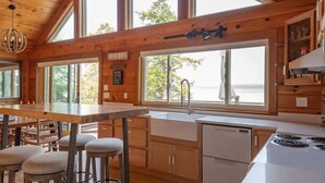 Eine geräumige Küche mit Holzsäulen, einer großen Kochinsel mit Hockern und Blick ins Freie.