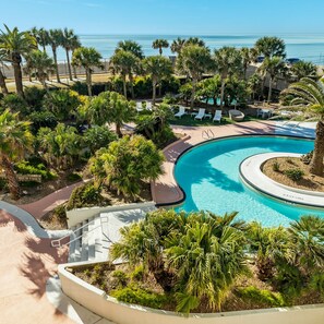 Une piscine d’hôtel au design incurvé, entourée de palmiers et de chaises longues.