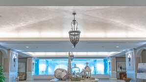 Un vestíbulo amplio con una fuente central, un candelabro y un gran ventanal con vistas al cielo.