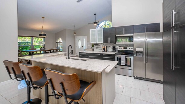 A modern kitchen with a large island, stainless steel appliances, and a dining area with bar stools. - Swiss 49 - Lake Denise (Clermont)