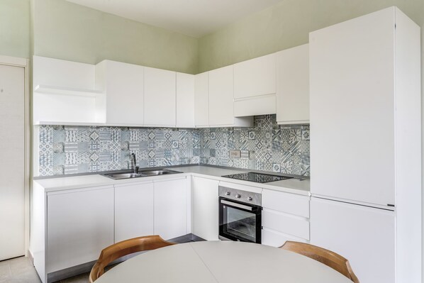 A compact kitchen with white cabinetry, a patterned backsplash, a built-in oven, and a refrigerator. - Le Arcate Sea La Vie (Massa Lubrense)