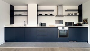 A modern kitchen with dark cabinetry, a white countertop, and built-in appliances including a microwave, oven, and coffee maker. - Manchester Industrial by Casacity (Manchester)