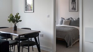 A room with a wooden dining table, black chairs, a potted plant, and a bed with a grey blanket and pillows. - Manchester Industrial by Casacity (Manchester)