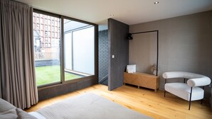 Une chambre moderne avec une grande fenêtre, un lit, un banc et une chaise.