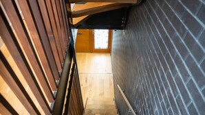Un escalier en bois avec une rampe en métal, menant à une pièce dont un mur est en briques et qui possède une fenêtre.