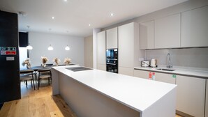 Une cuisine moderne dotée d’un grand îlot central, d’appareils électroménagers intégrés et de luminaires suspendus.