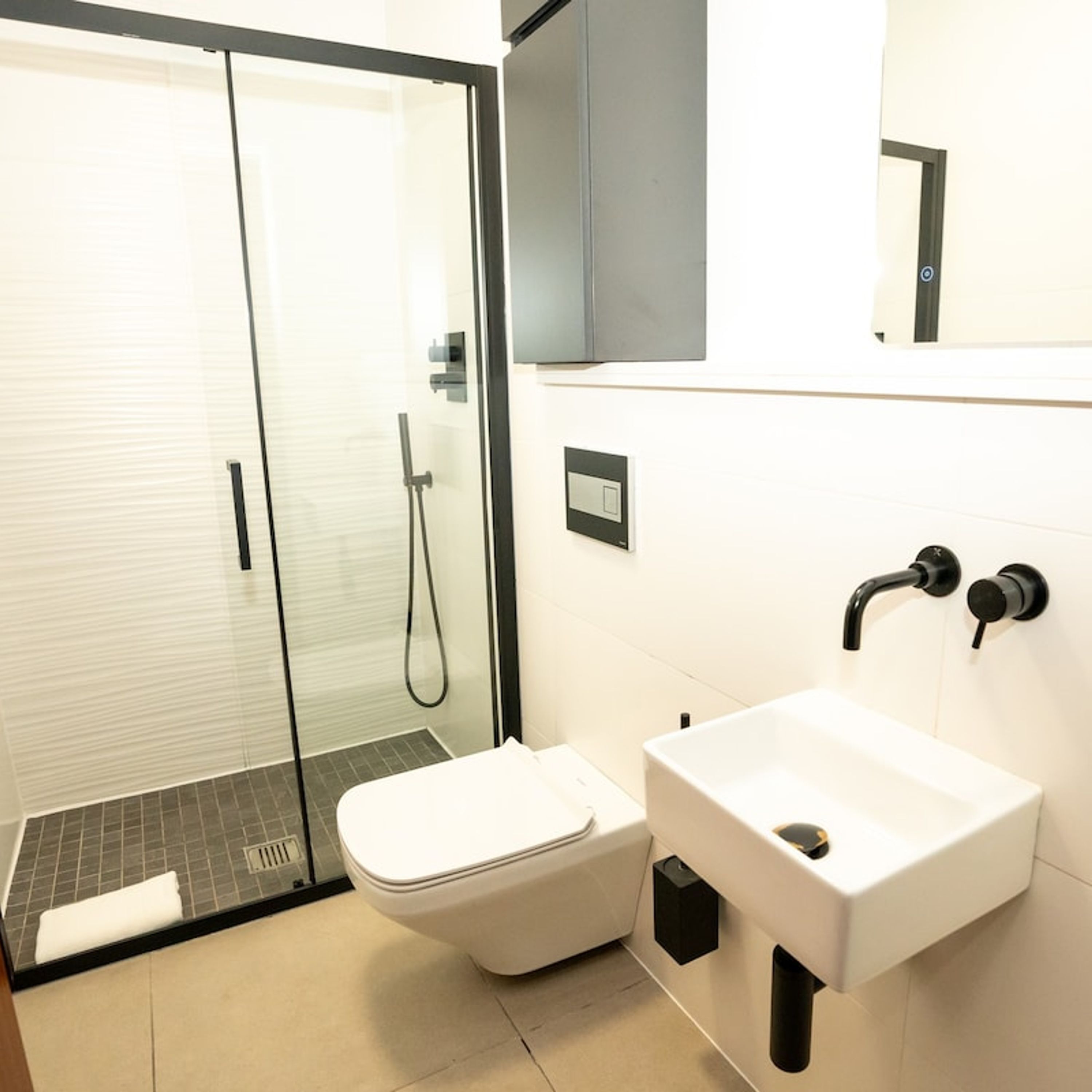 A modern bathroom with a glass shower enclosure, a white toilet, and a sink with a black faucet.