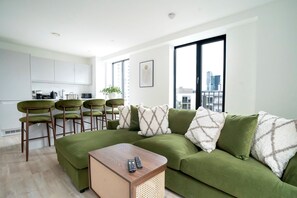 Un salon moderne avec un canapé vert, une table basse en bois et un coin cuisine doté de meubles blancs et de chaises vertes.