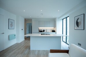 Una cocina moderna con armarios blancos, una isla central y vistas amplias a través de grandes ventanales.