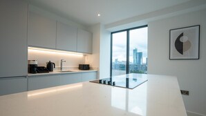 A modern kitchen with a large island, a view of the city, and minimalist cabinetry. - Alabaster Suite by Casacity (Salford)
