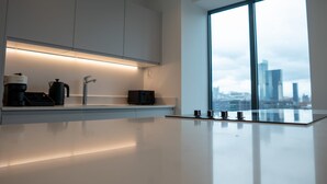 Une cuisine moderne au design minimaliste, dotée d’un plan de travail élégant, de meubles encastrés et d’une grande fenêtre offrant une vue sur la ville.