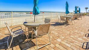 Eine Terrasse direkt am Strand mit Tischen, Stühlen, einer Geländer und Sonnenschirmen.