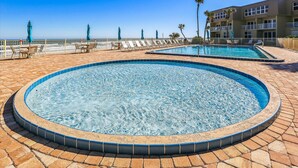 Ein Pool mit Fliesenrand, Liegestühlen und Meerblick.