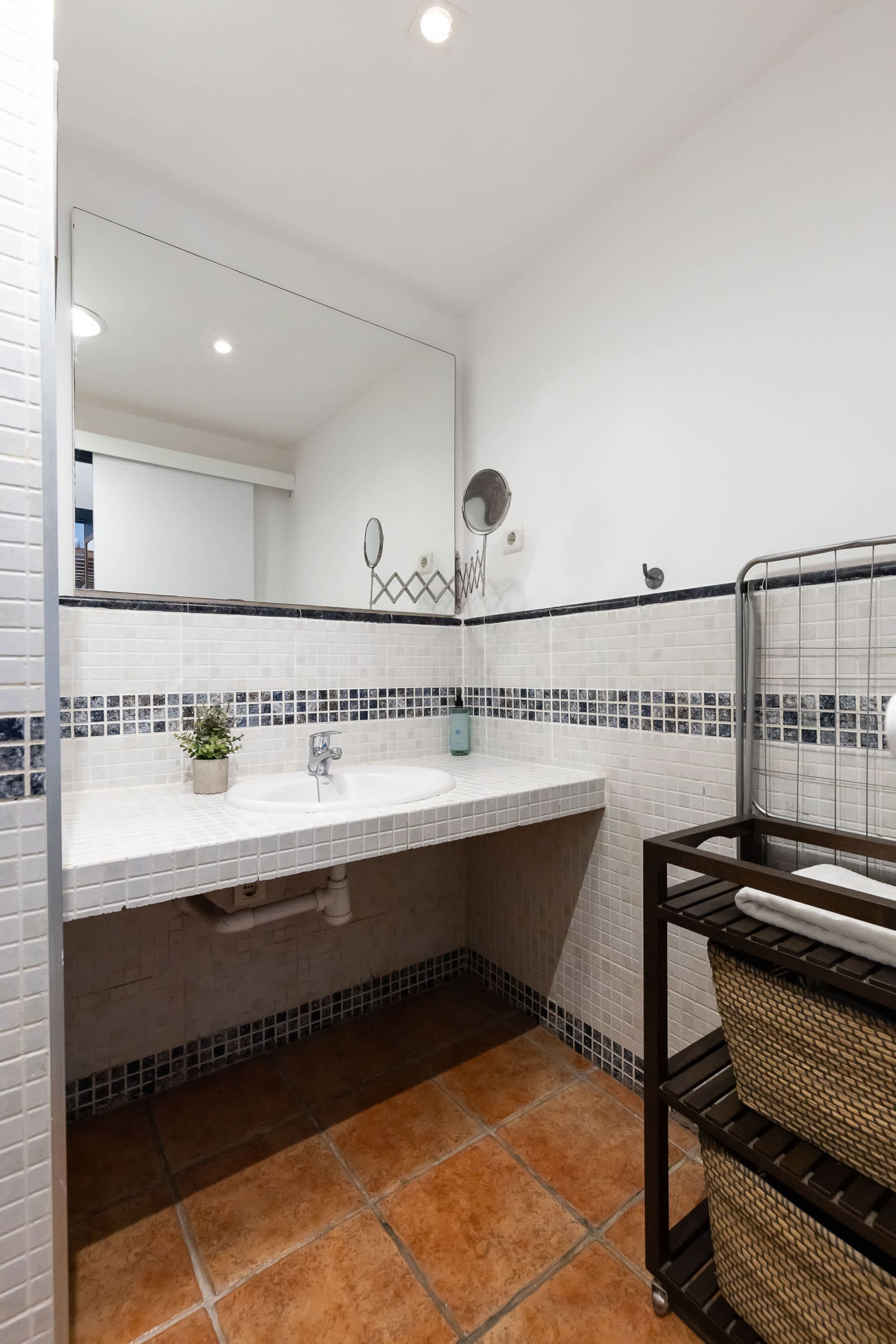 A bathroom with white tiled walls, a white sink, a mirror, a towel rack, and a small potted plant.