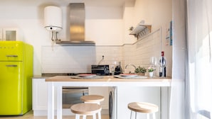 A modern kitchen with a bright yellow refrigerator, a built-in oven, a microwave, and a sink. There are two wooden stools under the counter. - Unik Vacation Oli in Tarragona (Tarragona)