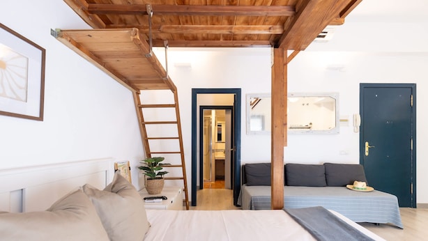 A bedroom with a bed, a sofa, a ladder, a potted plant, and a door. - Unik Vacation Oli in Tarragona (Tarragona)