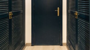 A black door with a brass handle, flanked by two black louvered doors, in a hallway with light wooden flooring. - Unik Vacation Oli in Tarragona (Tarragona)