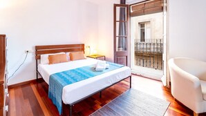 Hotellihuone, jossa on sänky, tuoli, yöpöytä, ikkuna ja ovi, joka johtaa parvekkeelle.