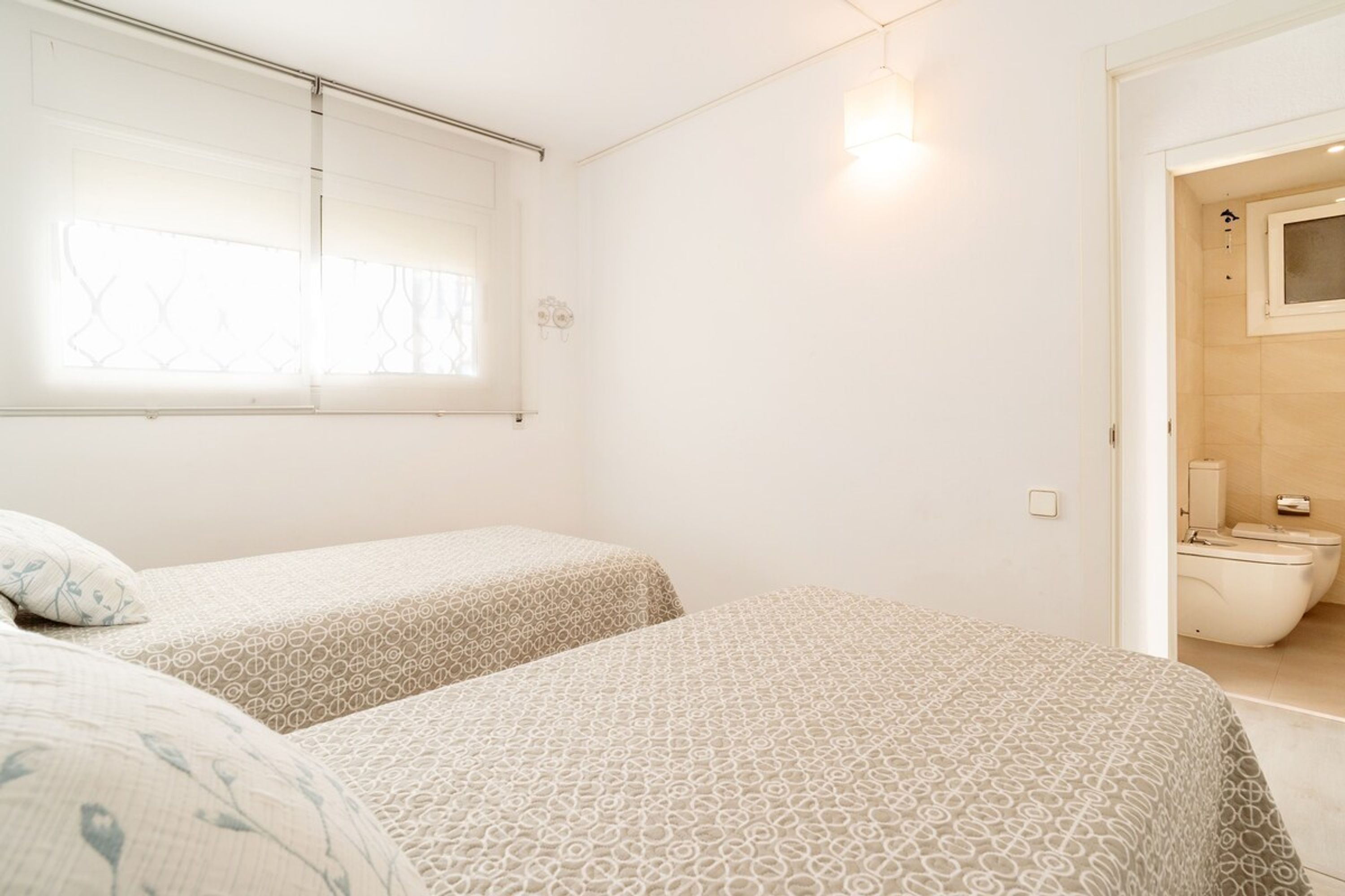 Ein Zimmer mit zwei Betten, einem Fenster mit Jalousien, einer Toilette und einer Dusche.