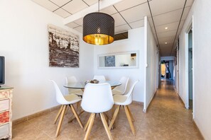 A modern dining area with a glass table, white chairs, and a pendant light. - Unik Vacation Rovellat (Tarragona)