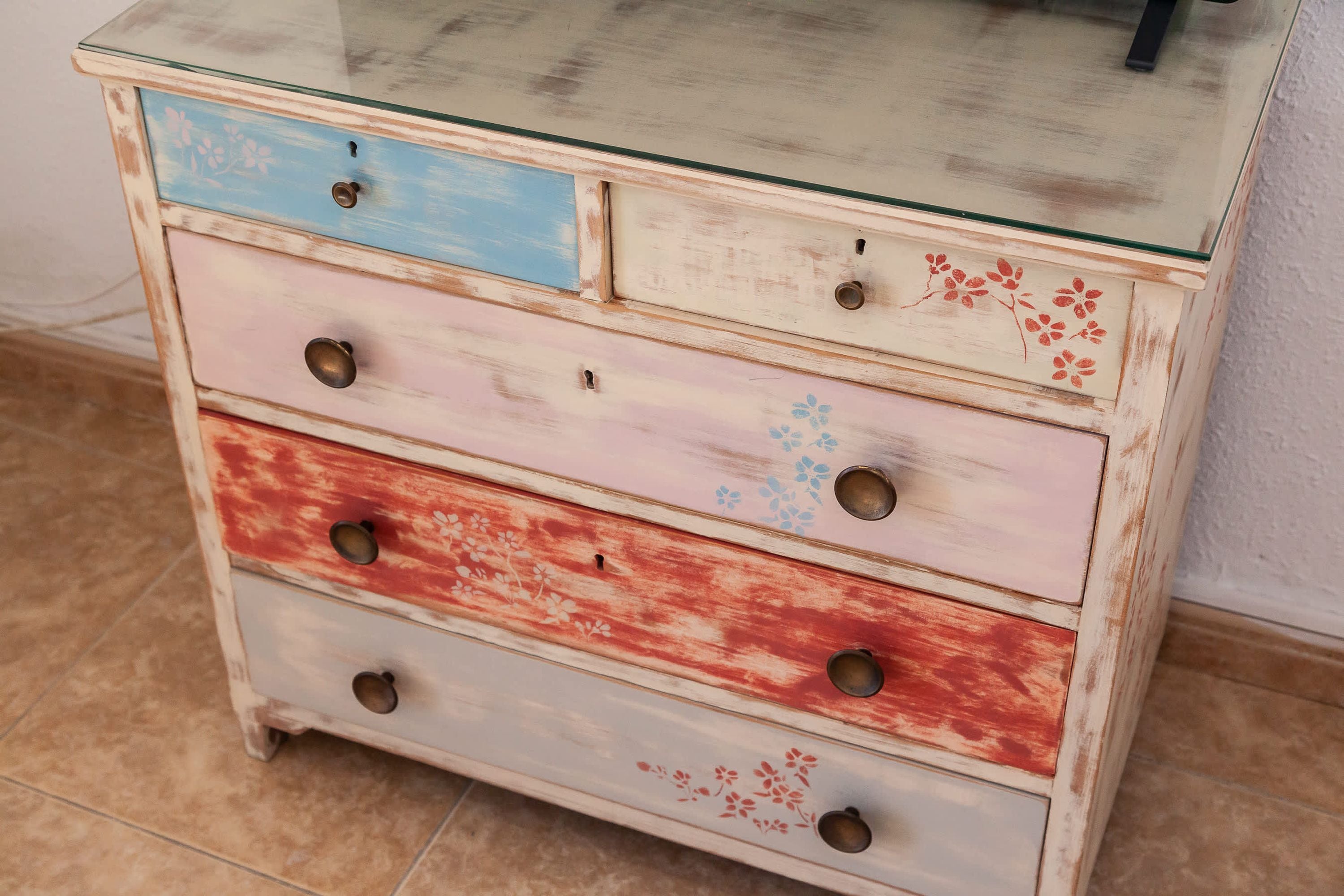A multi-drawer wooden dresser with glass top and metal handles.