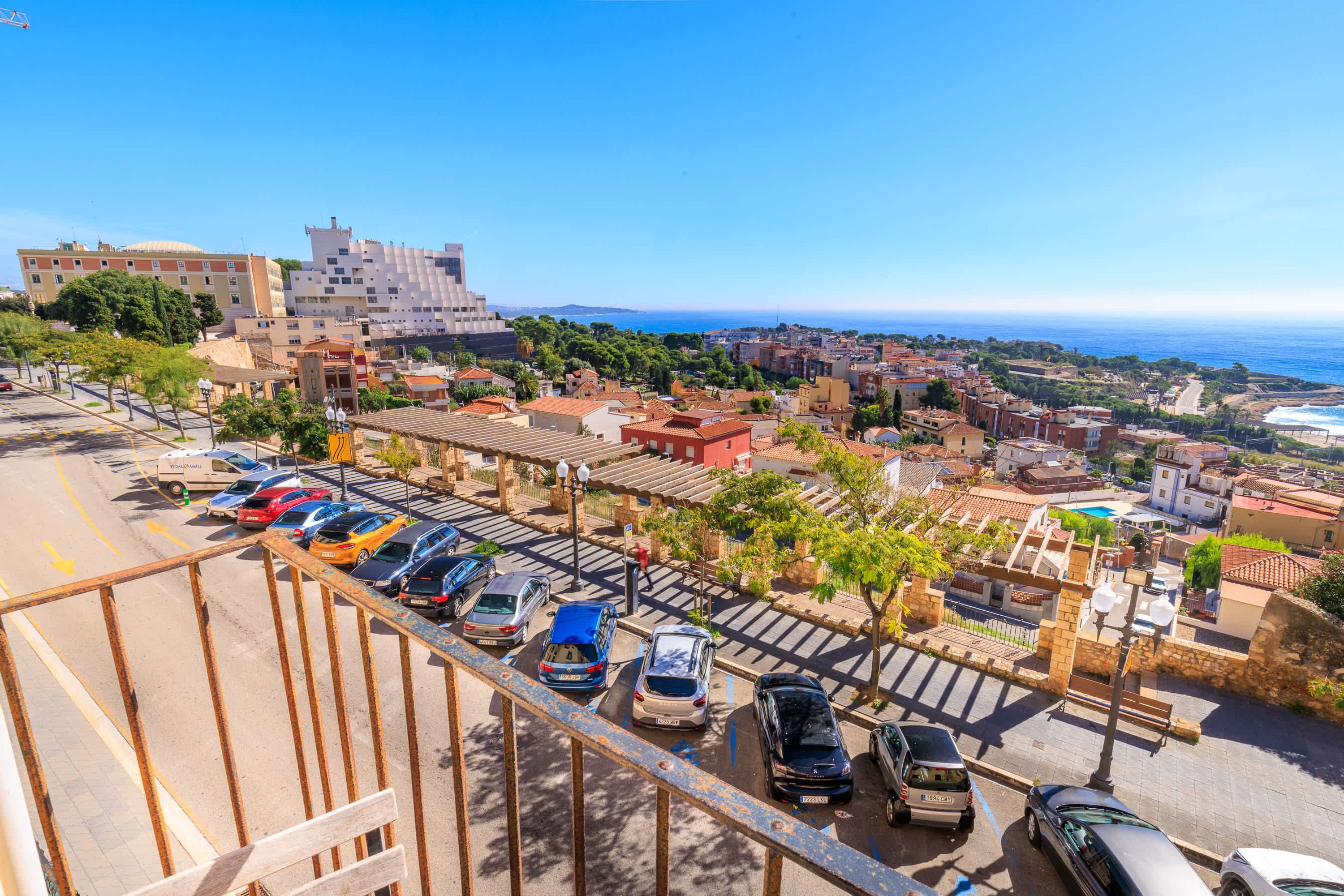 A coastal cityscape with a parking area, buildings, and a view of the sea.