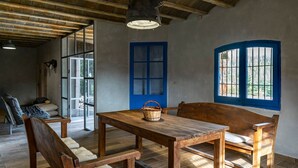 Una stanza rustica con un tavolo e panche in legno, una finestra con cornice blu e un lampadario.