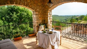 Un balcone in pietra con un tavolo apparecchiato per mangiare, circondato da piante in vaso e vista sulla campagna.