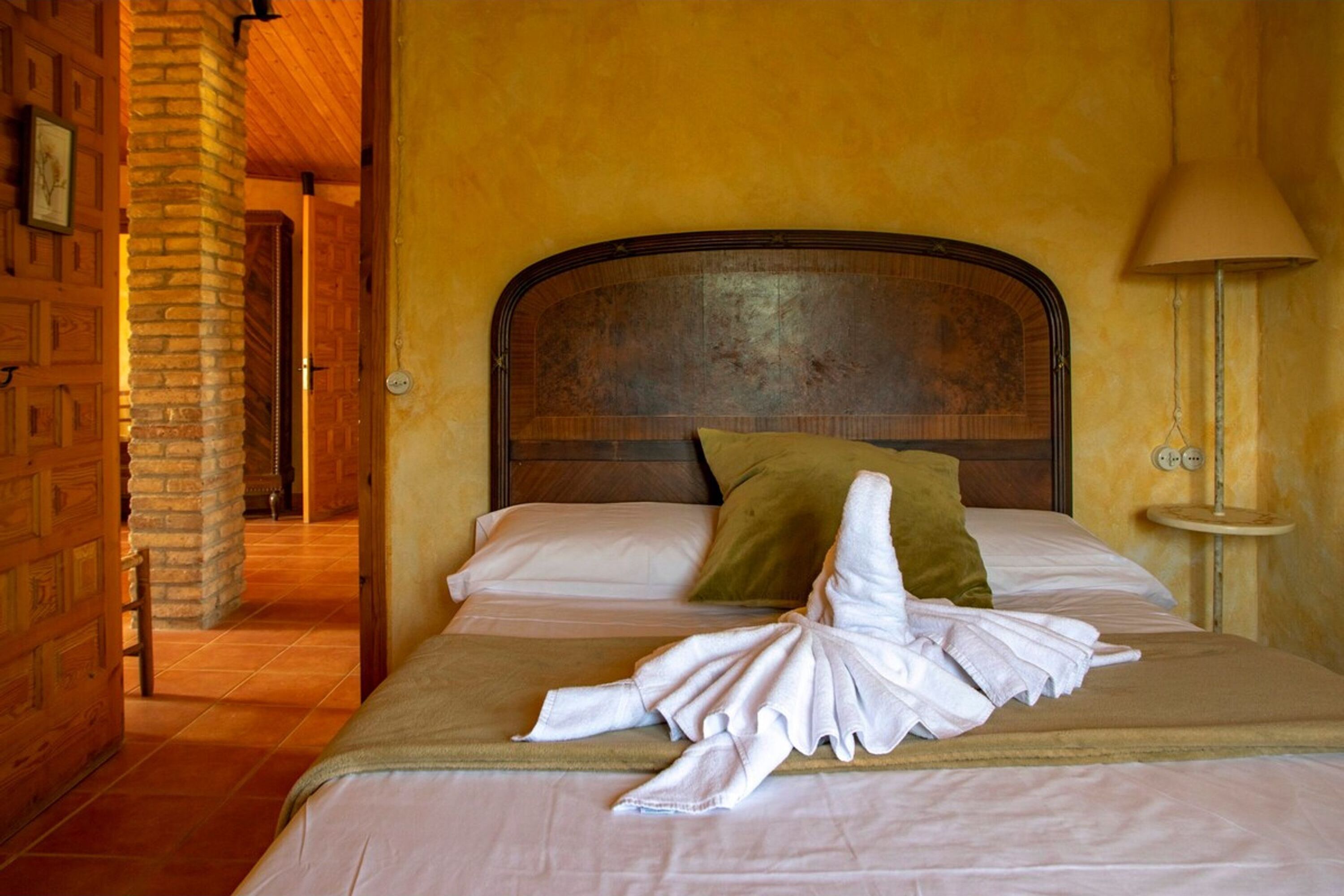 Habitación de hotel con una cama, cabecera de madera, almohada verde y una toalla sobre la cama.