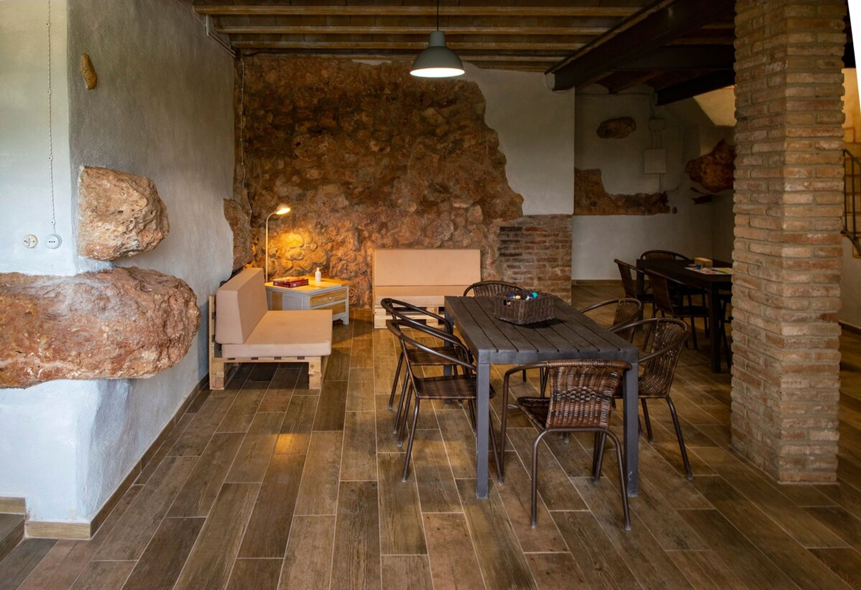 Un comedor rústico con pared de piedra, mesa de madera y sillas de mimbre.