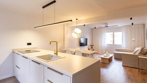 A modern kitchen with white cabinetry, a central island with a sink, and pendant lighting. - Unik Vacation Train Station (Tarragona)