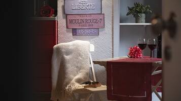 Una habitación acogedora con un letrero antiguo, una pequeña mesa con copas de vino tinto y un sillón con una manta tejida.