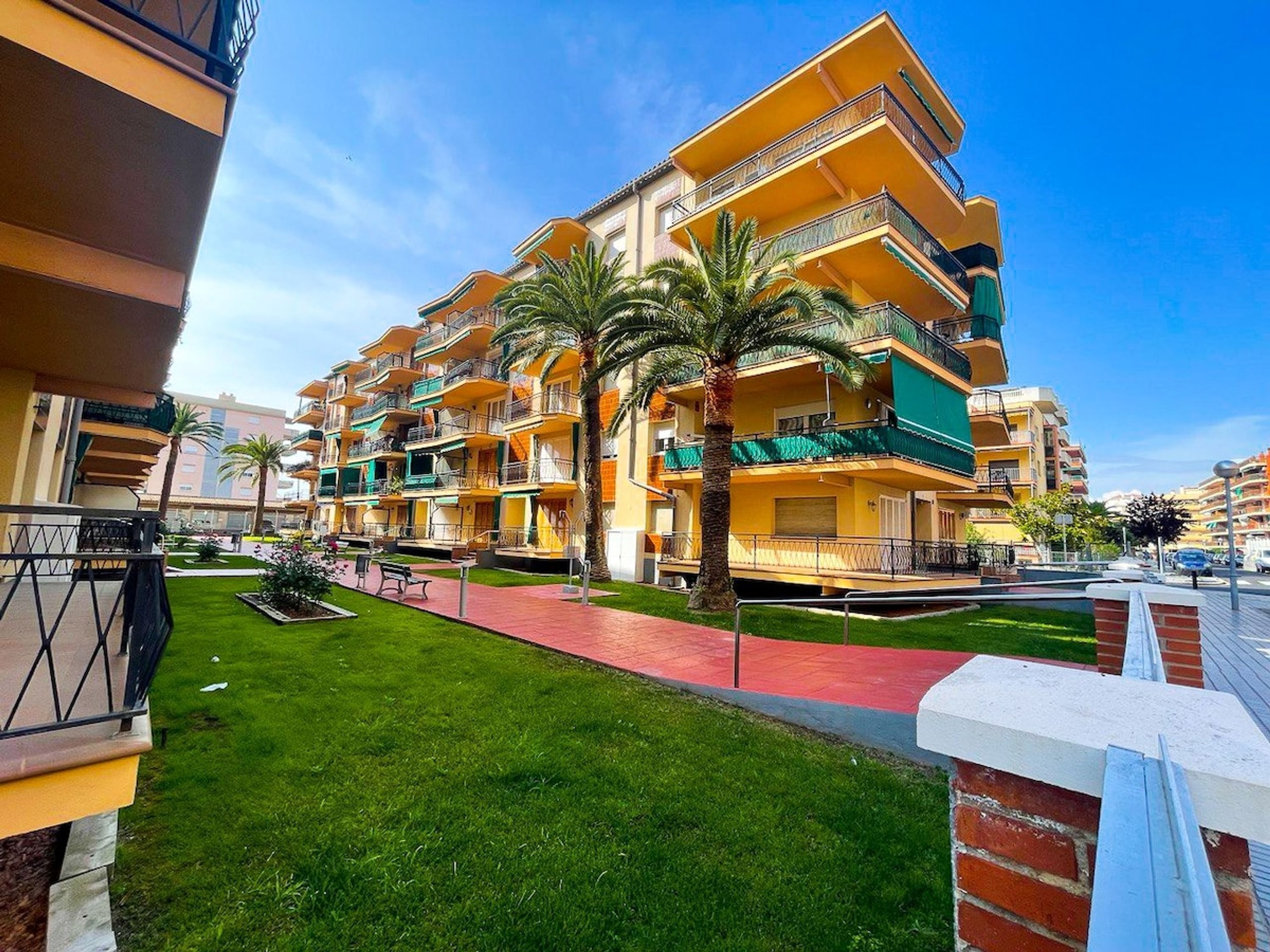 A multi-story hotel with balconies, a red pathway, and green landscaping.