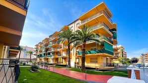 A multi-story hotel with balconies, a red pathway, and green landscaping. - Unik Vacation Palm Beach (Vila-Seca)