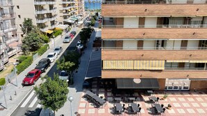 A multi-story building with balconies, a street with parked cars, and outdoor seating. - Unik Vacation Palm Beach (Vila-Seca)