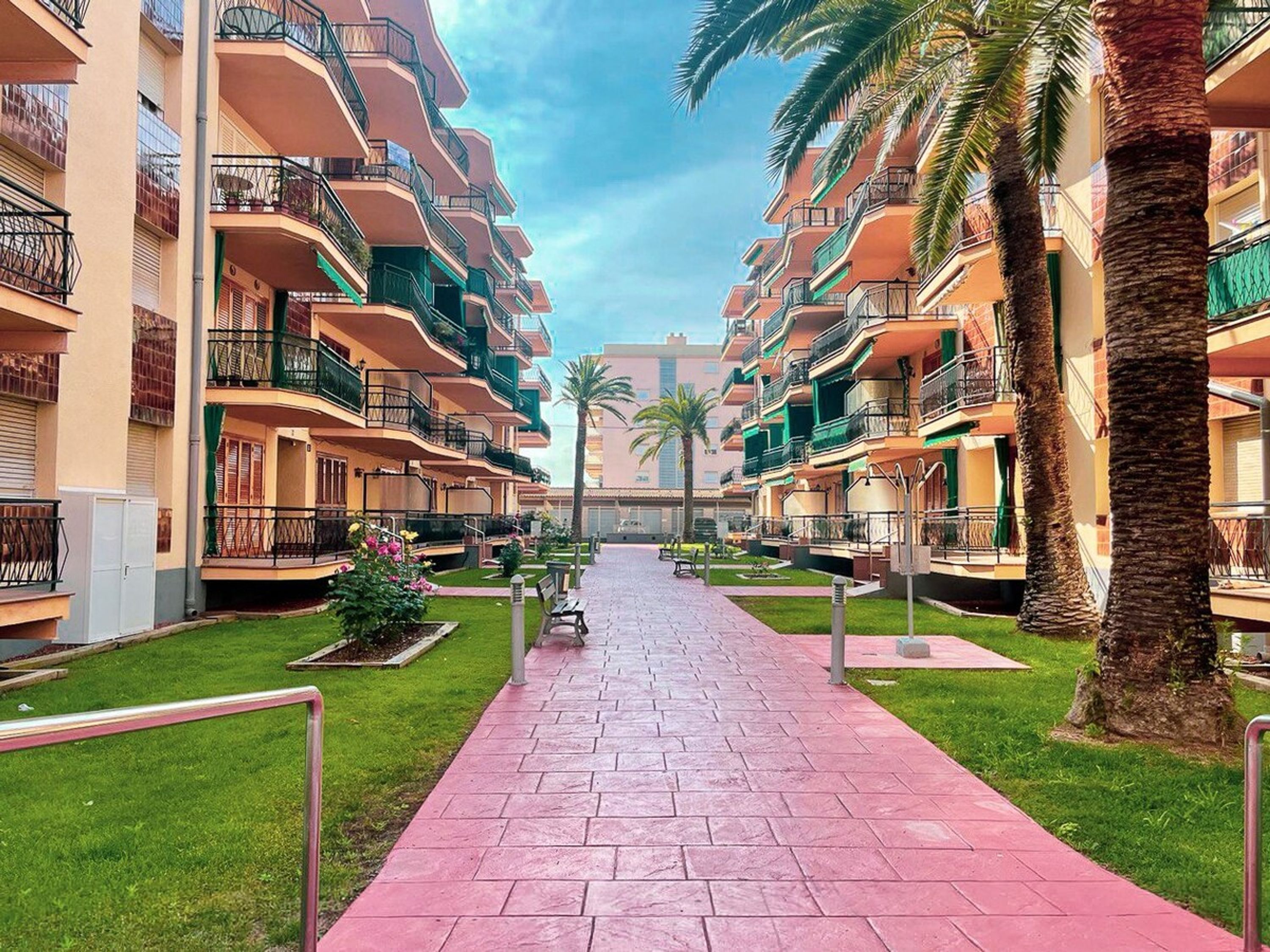 A multi-story hotel with balconies, a central walkway, and palm trees.