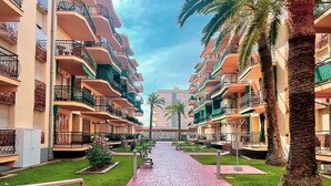 A multi-story hotel with balconies, a central walkway, and palm trees. - Unik Vacation Palm Beach (Vila-Seca)