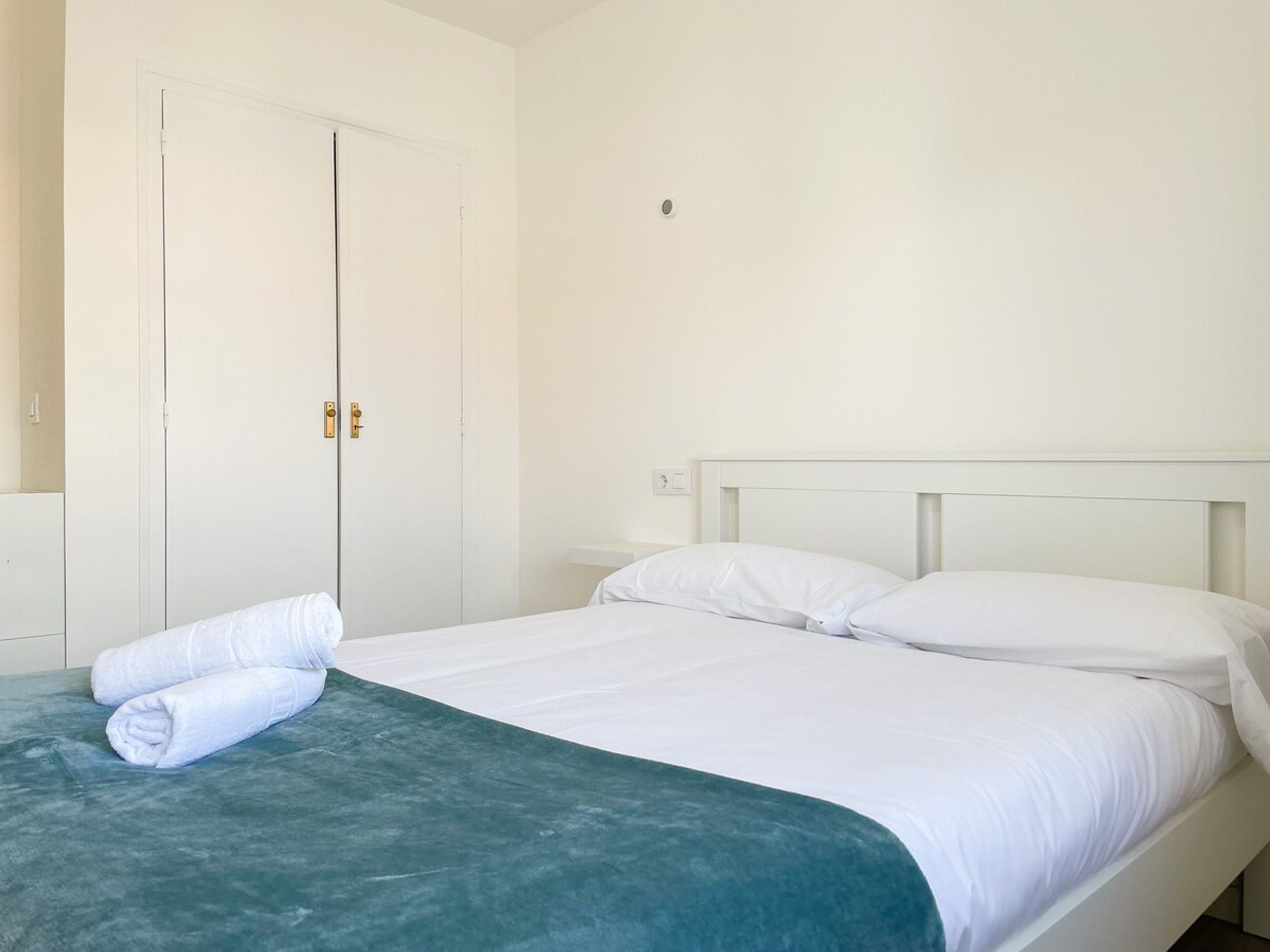 A single bed with white bedding, a teal-colored bedspread, and a white headboard.