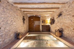 A stone-walled room with a glass floor, wooden door, and a small cabinet with a lamp. - Unik Vacation Ca La Lola (Nulles)