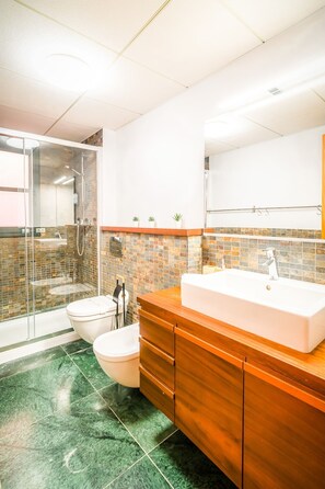 A modern bathroom with a glass-enclosed shower, a white sink, and a tiled backsplash. - Unik Vacation Civaderia (Tarragona)
