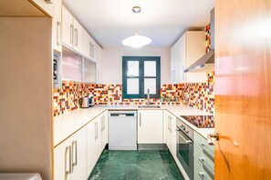 A compact kitchen with white cabinets, a tiled backsplash, and a green marble floor. - Unik Vacation Civaderia (Tarragona)