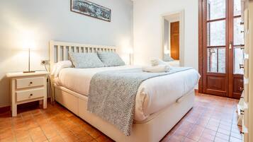 Ein Schlafzimmer mit Bett, Nachttischlampen, einem Nachttisch, einem Wandbild und einer Tür, die auf einen Balkon führt.