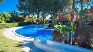 A swimming pool with a curved edge, surrounded by lush greenery and palm trees. - Unik Vacation Tamarit (Tarragona)