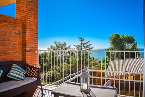 A balcony with a sofa and a table, a lantern, and a view of the sea and trees. - Unik Vacation Tamarit (Tarragona)