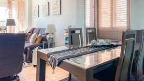 A modern living room with a sofa, dining table, and chairs. There is a lamp on a side table, and artwork on the wall. - Unik Vacation Tamarit (Tarragona)