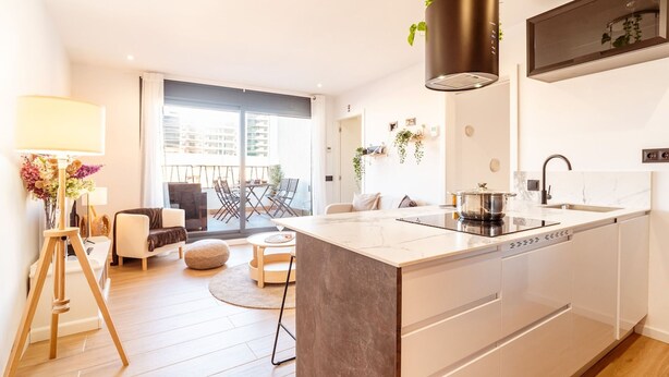 A modern kitchen with a central island, a dining area with a round table, and a balcony with a view of the city. - Unik Vacation Penthouse (Tarragona)